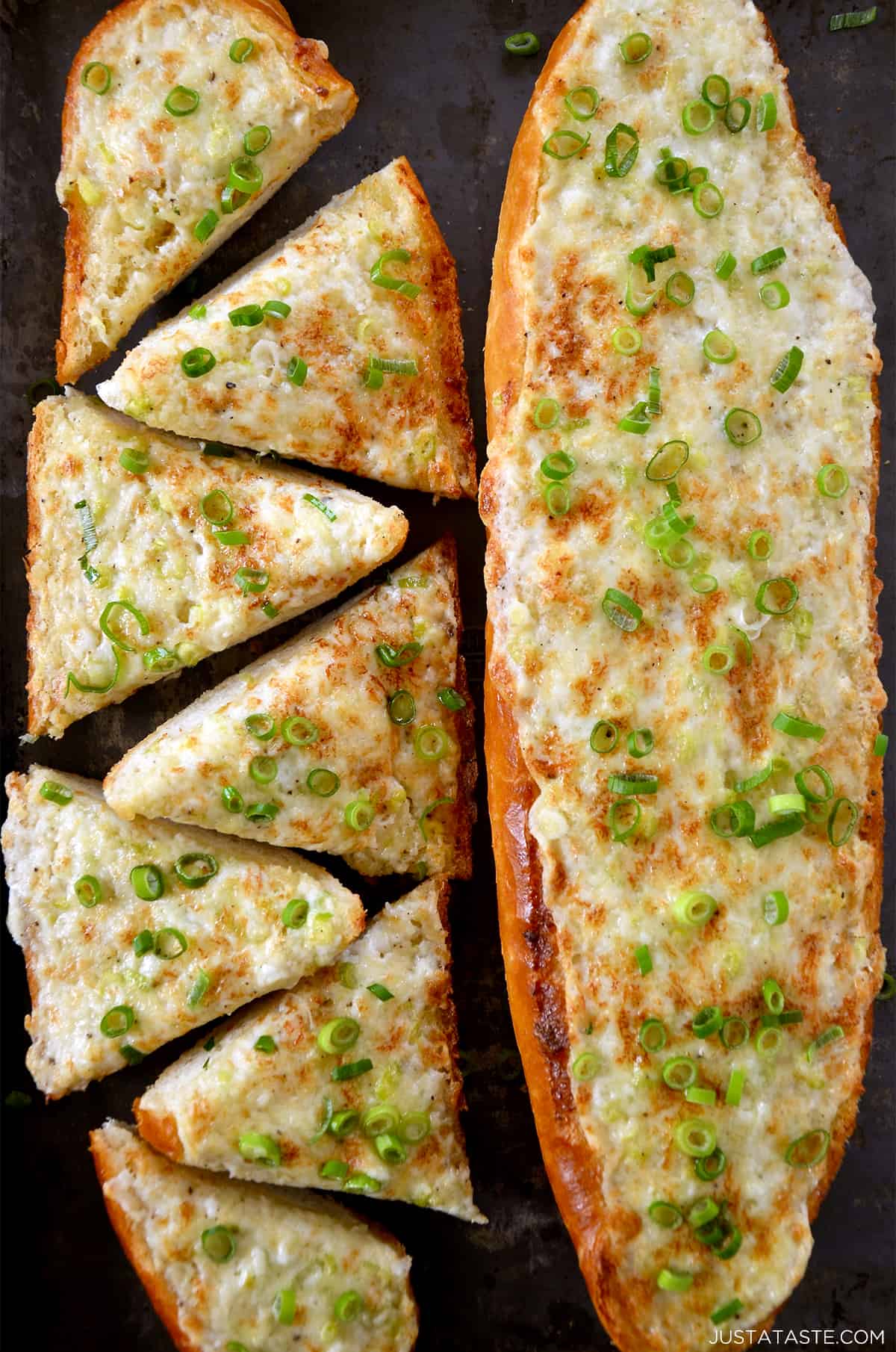 Two cheesy garlic bread loafs topped with sliced scallions.