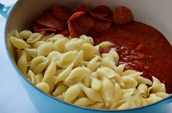 Closeup view of Conchiglie, marinara sauce and pepperoni in large blue stockpot