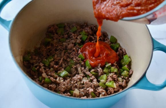 Marinara sauce being poured over ground Italian sausage in stockpot