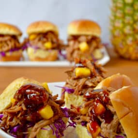 Three slider buns on a plate piled high with Slow Cooker Hawaiian Pulled Pork drizzled with barbecue sauce