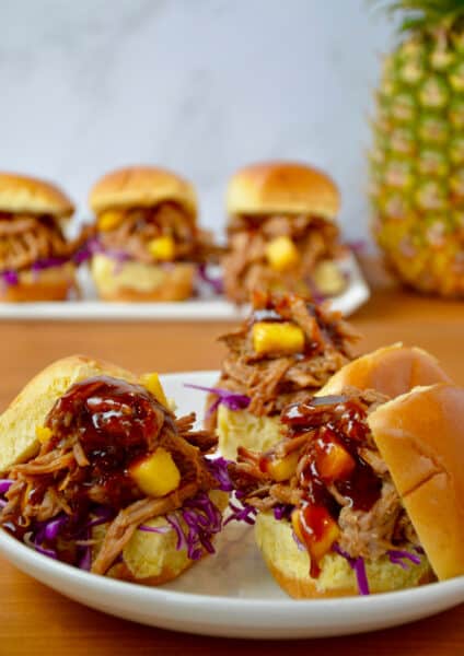 Three slider buns on a plate piled high with Slow Cooker Hawaiian Pulled Pork drizzled with barbecue sauce