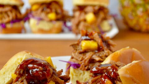 Three slider buns on a plate piled high with Slow Cooker Hawaiian Pulled Pork drizzled with barbecue sauce