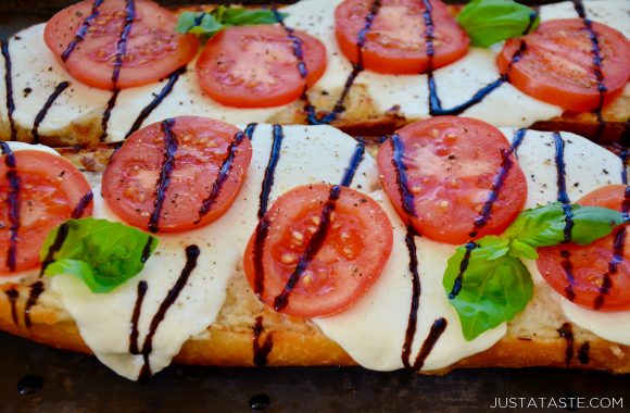 Two halves of Caprese Garlic Bread topped with mozzarella cheese, fresh tomatoes and basil, and drizzled with balsamic syrup 