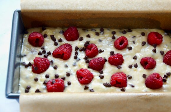 A loaf containing banana bread batter topped with raspberries and chocolate chips