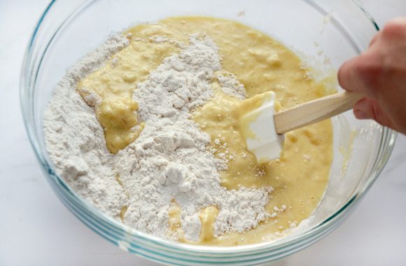 A glass bowl containing banana bread batter being stirred with a white spatula