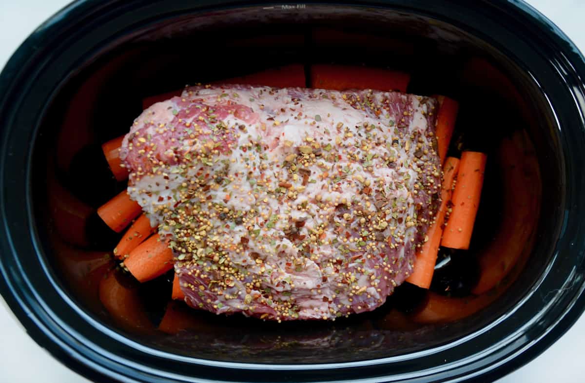 Corned beef sits on a bed of carrots in a slow cooker crock.