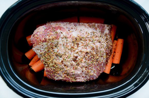 Top view of slow cooker containing corned beef brisket on top of carrots