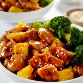 White bowl containing Sheet Pan Pineapple Chicken and Broccoli garnished with sesame seeds