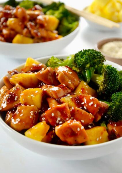 White bowl containing Sheet Pan Pineapple Chicken and Broccoli garnished with sesame seeds