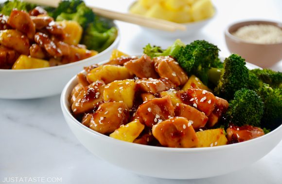 White bowl containing Sheet Pan Pineapple Chicken and Broccoli with another bowl and chopsticks in background