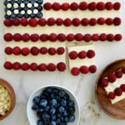 A top-down view of an American flag cookie cake with cream cheese frosting, raspberries, blueberries and white chocolate chips.