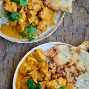 Two plates containing The Best Chicken Tikka Masala with cilantro, white rice and naan