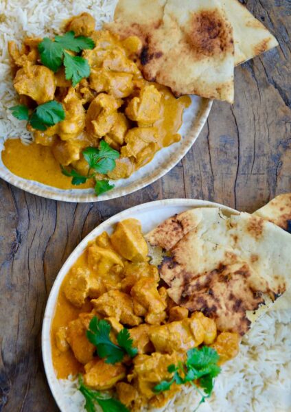 Two plates containing The Best Chicken Tikka Masala with cilantro, white rice and naan