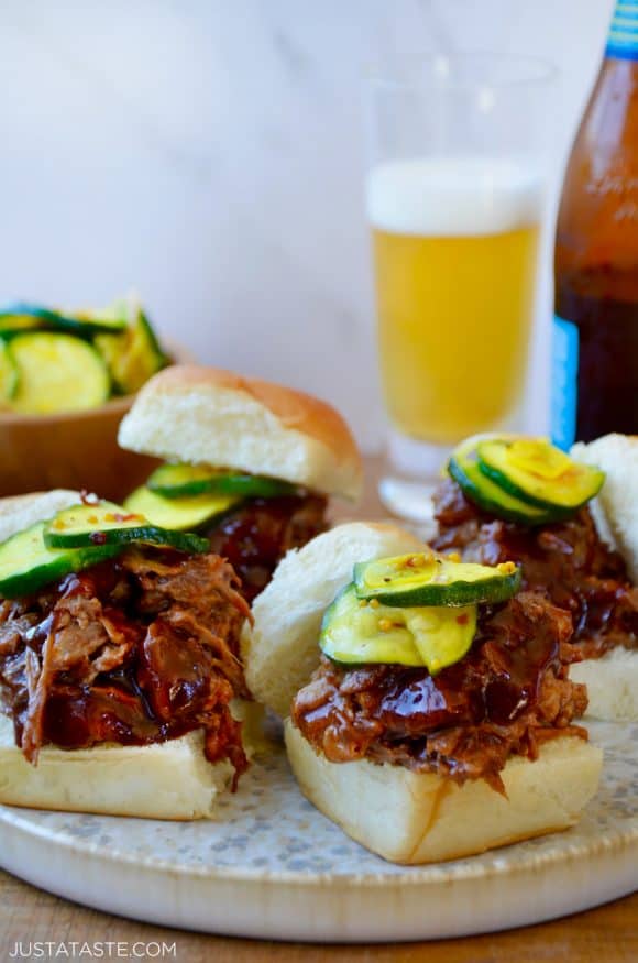 White buns piled high with Instant Pot Barbecue Pulled Pork and pickles in front of a bottle and glass of beer 