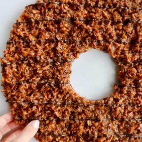 A top down view of a Giant Samoas Cookie Cake with a female hand touching it