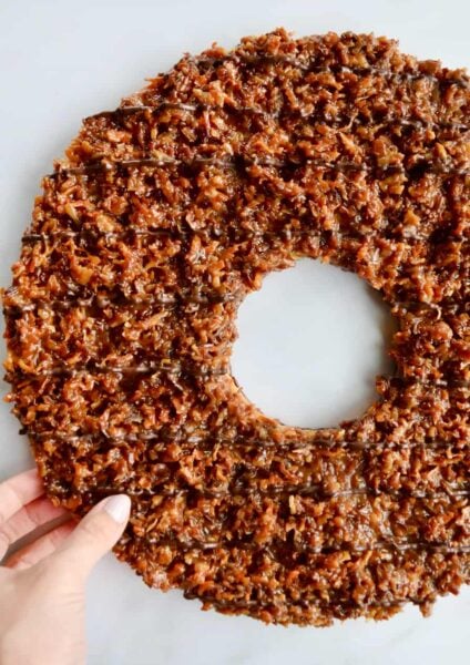 A top down view of a Giant Samoas Cookie Cake with a female hand touching it