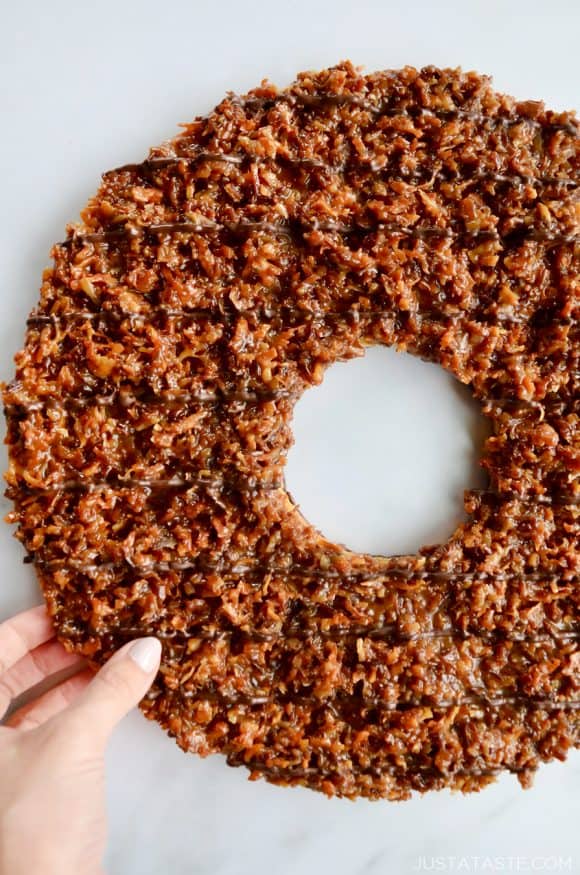 A top down view of a Giant Samoas Cookie Cake with a female hand touching it