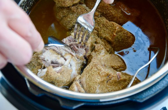 Two hands holding forks shredding cooked pork in an Instant Pot 