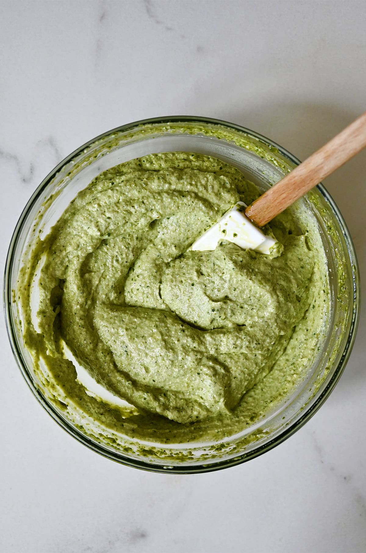 Pesto-ricotta cheese mixture in a glass bowl with a spatula.