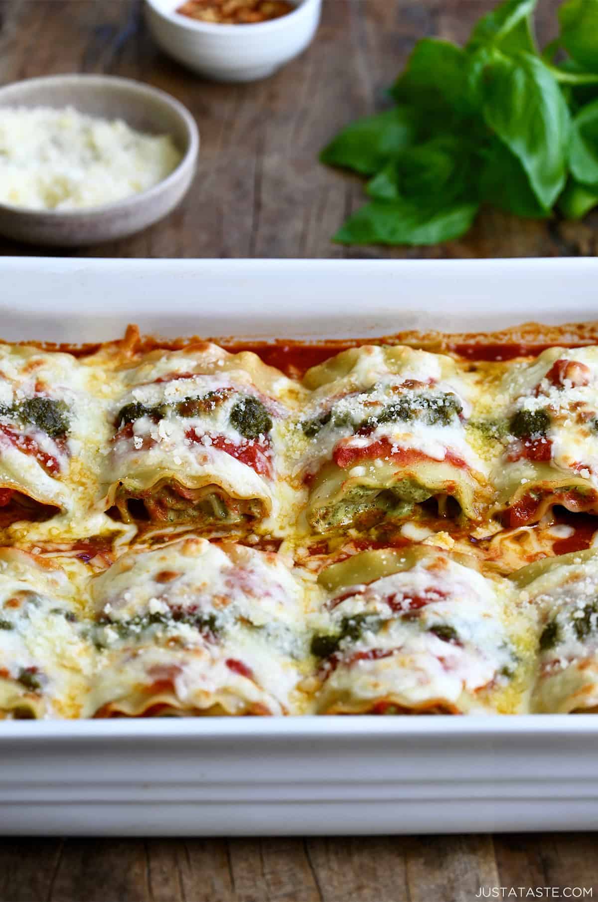 Lasagna roll-ups with pesto and marinara sauce in a white baking dish.