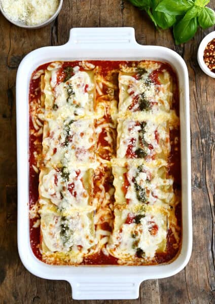 Easy lasagna roll-ups topped with pesto and mozzarella in a baking dish.