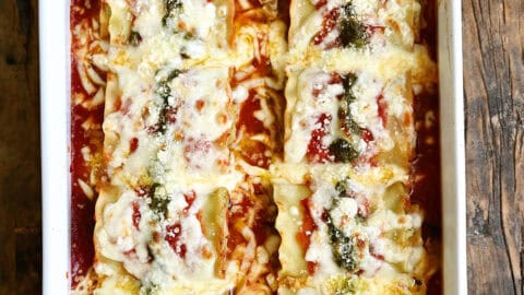 Easy lasagna roll-ups topped with pesto and mozzarella in a baking dish.