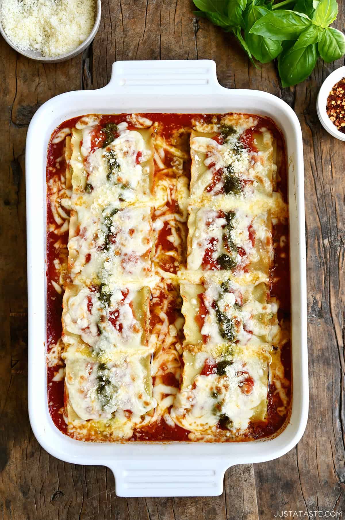 Easy lasagna roll-ups topped with pesto and mozzarella in a baking dish.