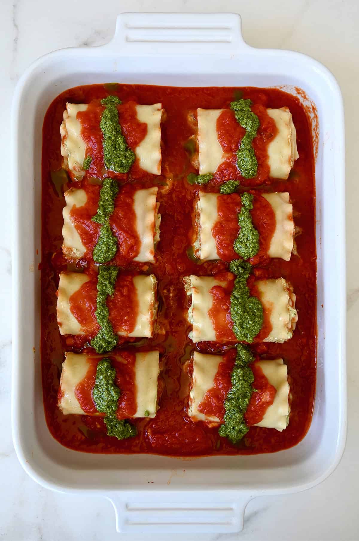 Lasagna roll-ups in a 9x13 baking dish topped with marinara sauce and pesto.