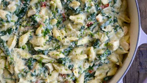 Top down view of a saucepot containing Spinach Artichoke Dip Pasta with Chicken next to an artichoke cut in half