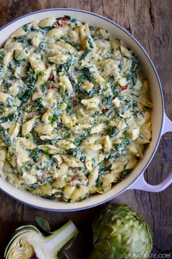 Top down view of a saucepot containing Spinach Artichoke Dip Pasta with Chicken next to an artichoke cut in half