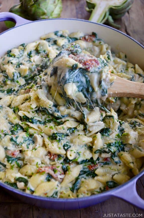 Saucepot containing the best Spinach Artichoke Dip Pasta with Chicken and wooden spoon