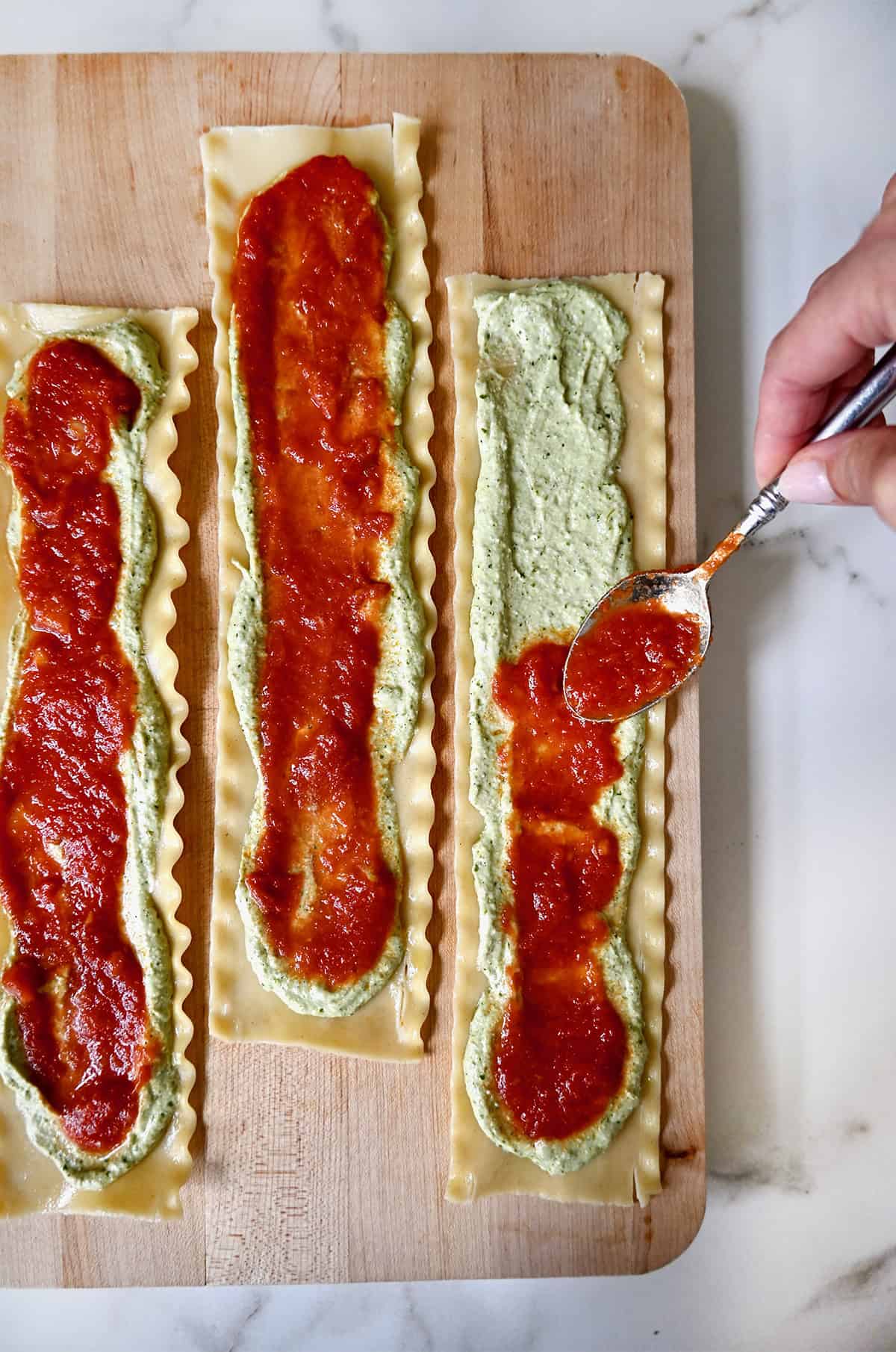 Three cooked lasagna noodles spread with pesto-ricotta and marinara sauce.