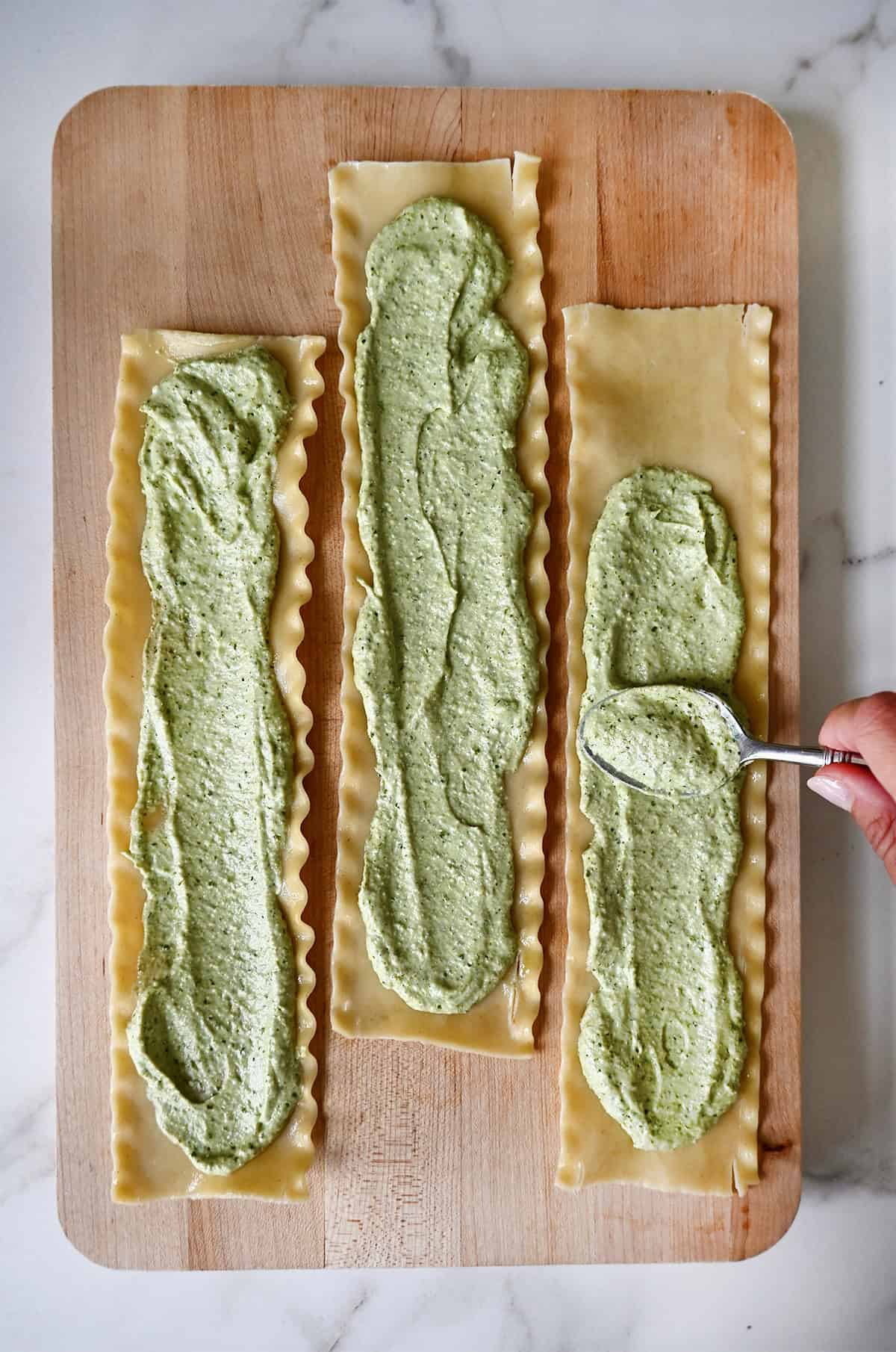 Three cooked lasagna noodles slathered with a pesto-ricotta mixture.