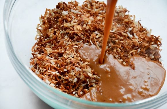 Glass bowl containing toasted coconut with melted caramel being poured on top