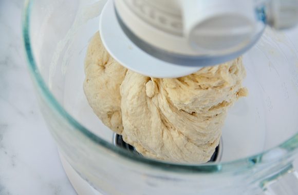 A clear glass mixing bowl containing homemade bagel dough