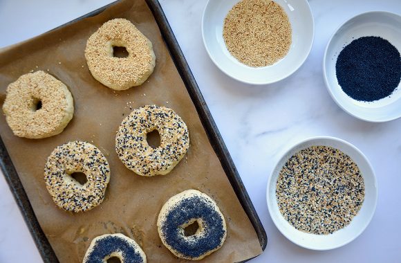 A baking sheet with unbaked bagels topped with seasonings