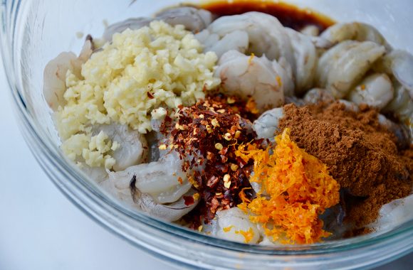 Glass bowl containing shrimp, minced garlic, chili flakes and spices