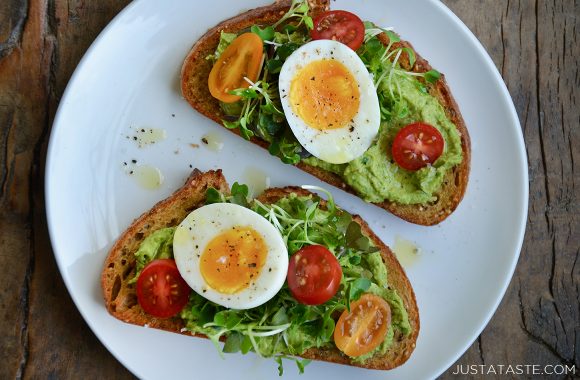 A white plate containing avocado hummus toast topped with jammy eggs