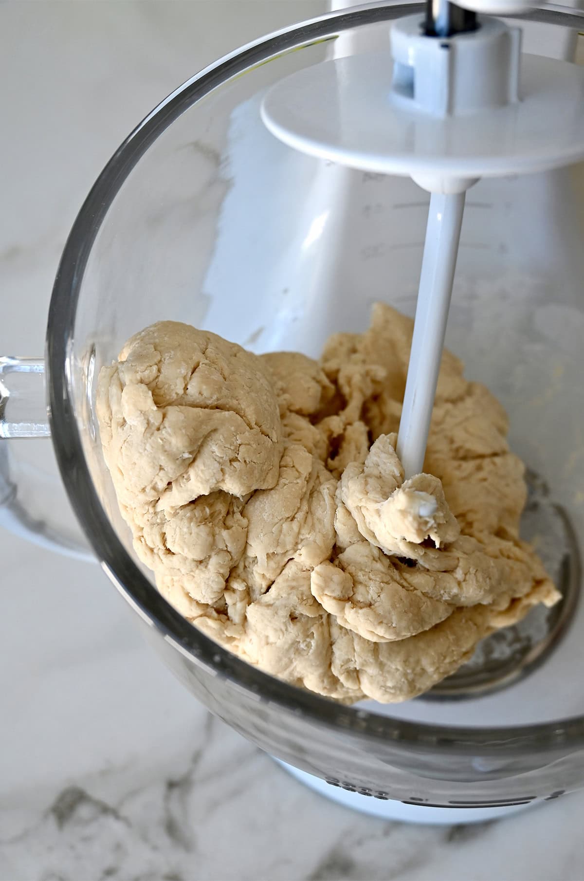 Bagel dough being kneaded by a stand mixer with the dough hook attachment.