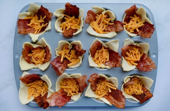 Muffin tin containing puff pastry filled with bacon and shredded cheese