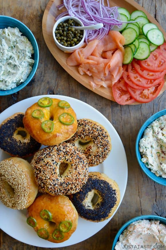 A white platter with homemade bagels surrounded by a lox platter and three bowls of cream cheese