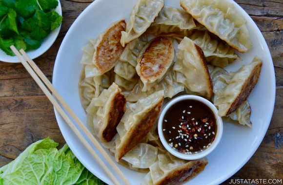 Pork Potstickers with Citrus-Soy Dipping Sauce on white plate with chopsticks next to bowl containing cilantro