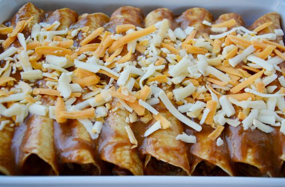 A baking pan filled with chicken enchiladas topped with cheese