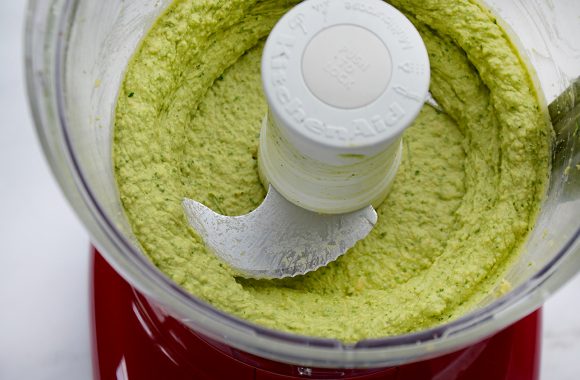 A clear food processor bowl containing avocado hummus