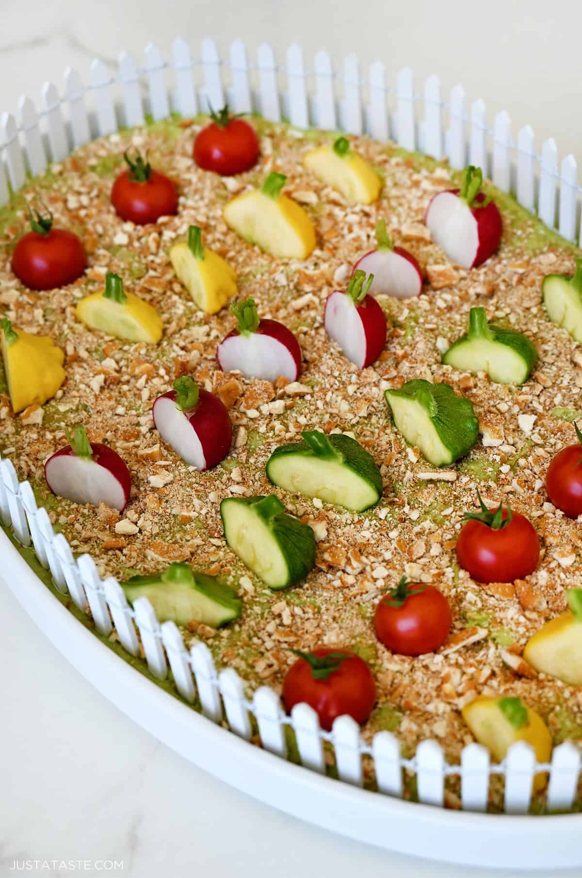 A platter containing avocado hummus topped with crushed pretzels and vegetables.