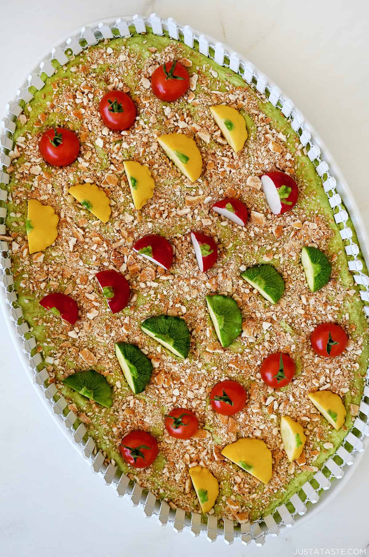 A platter containing avocado hummus topped with crushed pretzels and vegetables.