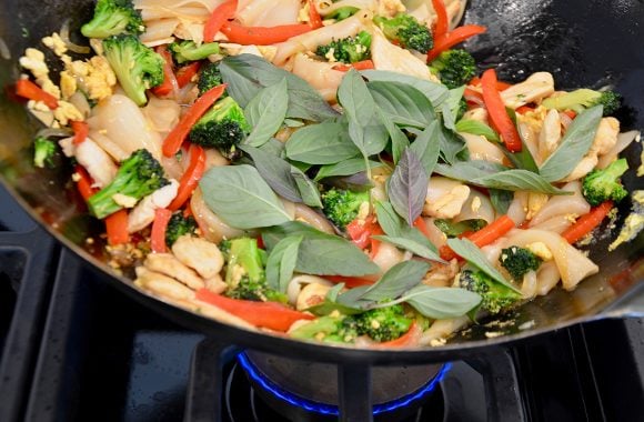 Wok containing chicken, red peppers and fresh thai basil