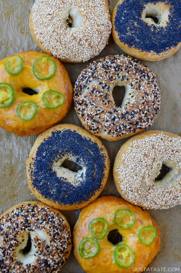A variety of homemade bagels topped with seasonings on brown parchment paper