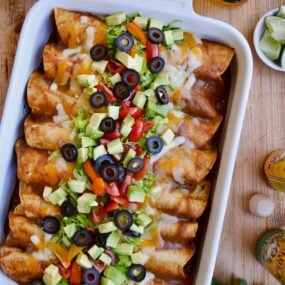 A white baking dish filled with enchiladas surrounded by beers