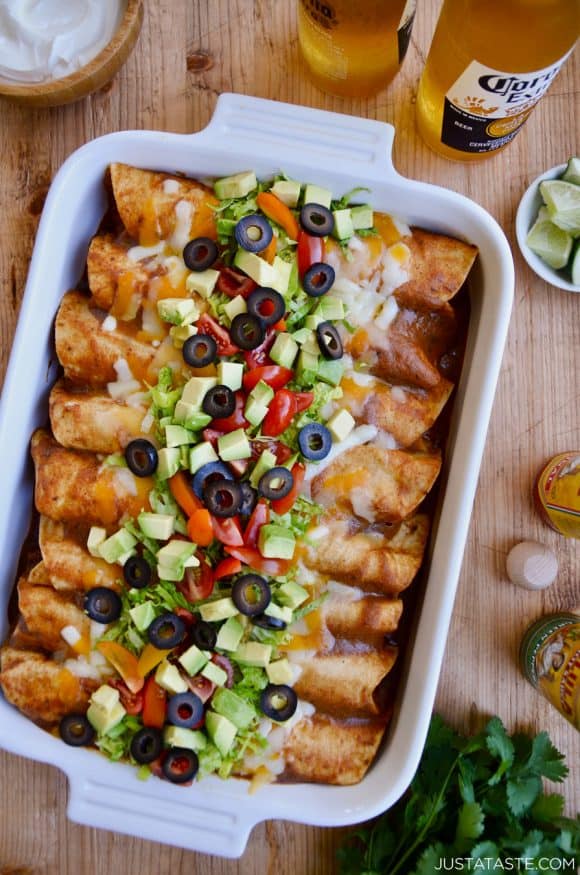 A white baking dish filled with enchiladas surrounded by beers